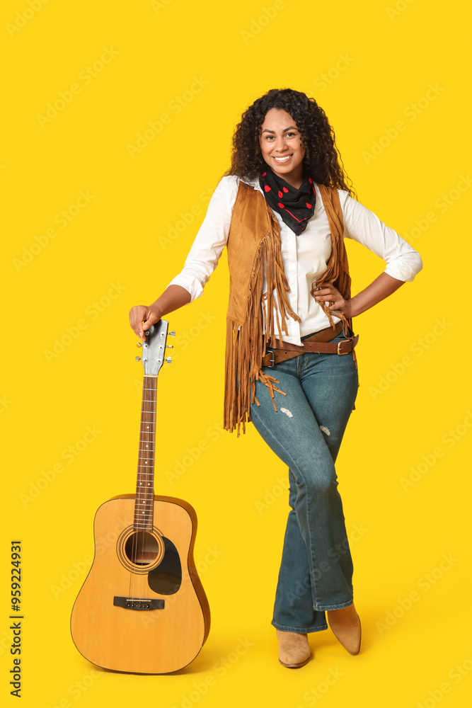 Beautiful African-American cowgirl with guitar on yellow background Beautiful African-American cowgirl with guitar on yellow background