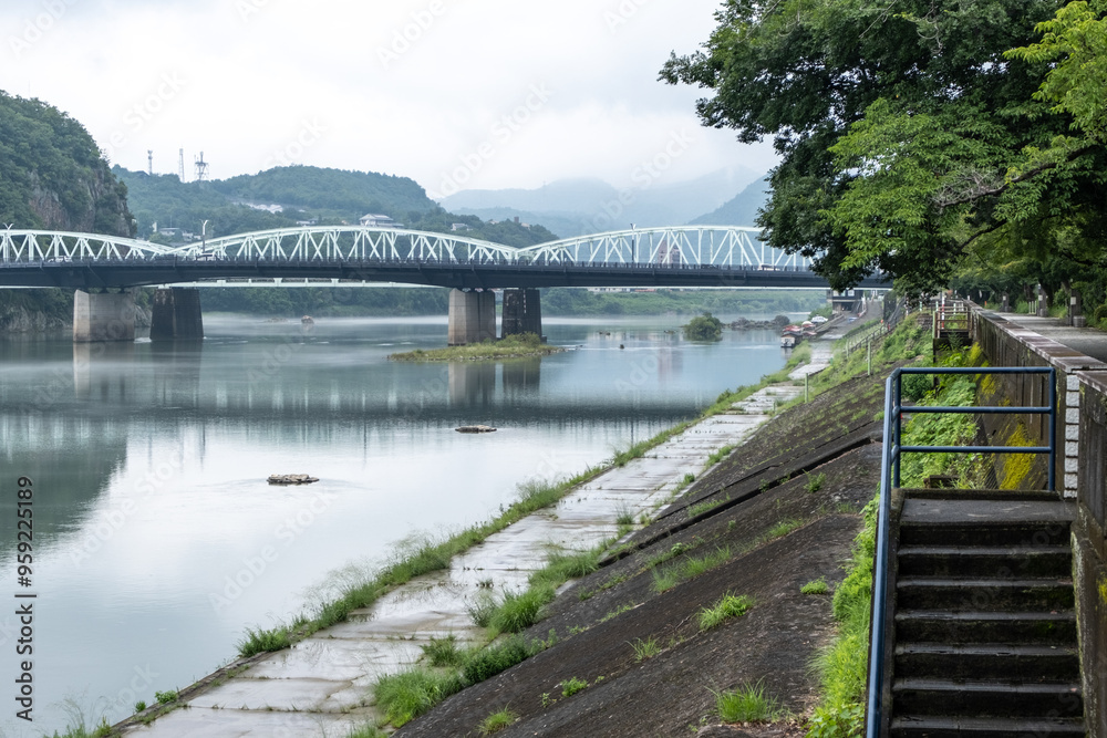 Obraz premium Peaceful and serene riverbank scenery of Kiso River in Japan with Inuyama Bridge over the water in the background. 犬山橋