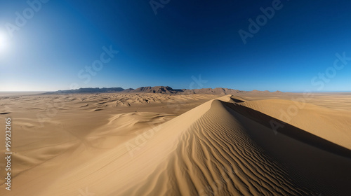 Vast desert landscape with tall sand dunes stretching towards distant mountains under a clear blue sky