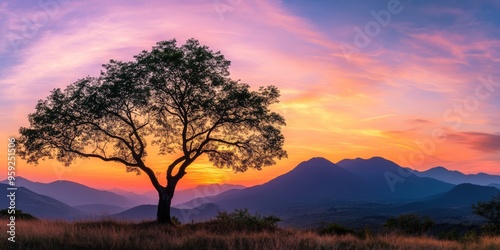 A serene landscape features a silhouetted tree against a vibrant sunset sky over distant mountains, creating an ideal sight for nature lovers who appreciate peaceful and calming scenery