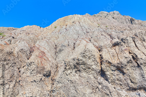 Rock wall showcasing rugged textures and natural formations under clear blue sky. Mountain is covered in rocks and has a rugged appearance