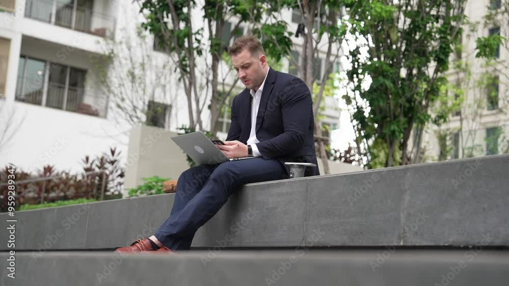 Skilled male leader working on his phone sending report while using laptop analyze investment data at green city. Happy investor looking marketing plan while sitting at park or eco urban city. Urbane. Skilled male leader working on his phone sending report while using laptop analyze investment data at green city. Happy investor looking marketing plan while sitting at park or eco urban city. Urbane.