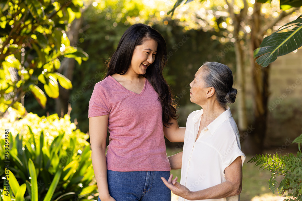 Smiling granddaughter talking with asian grandmother in garden, enjoying conversation Smiling granddaughter talking with asian grandmother in garden, enjoying conversation