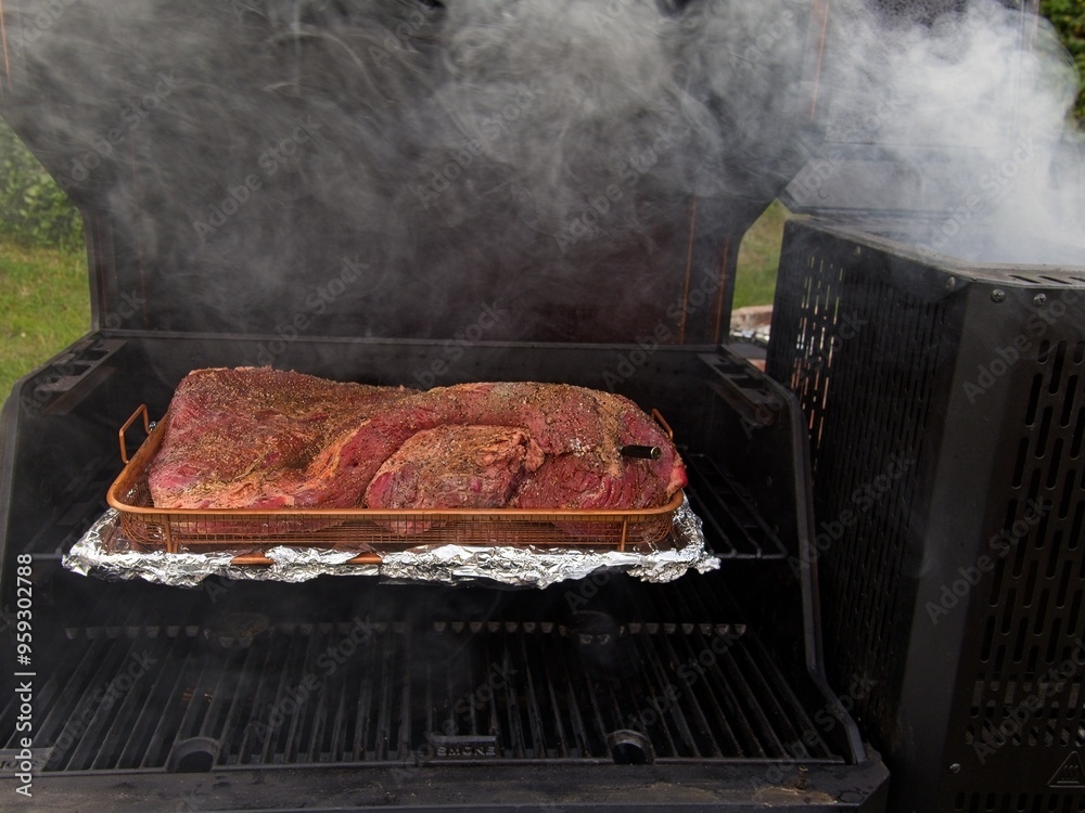 Packer brisket on a smoker in preparation for a low and slow cook, thick smoke coming from a smoker