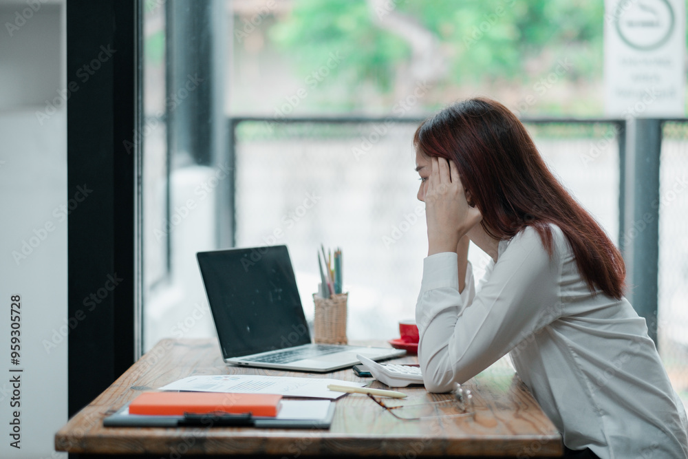 Young woman in white shirt working on a laptop at a wooden desk with natural light and greenery visible through the window. Young woman in white shirt working on a laptop at a wooden desk with natural light and greenery visible through the window.