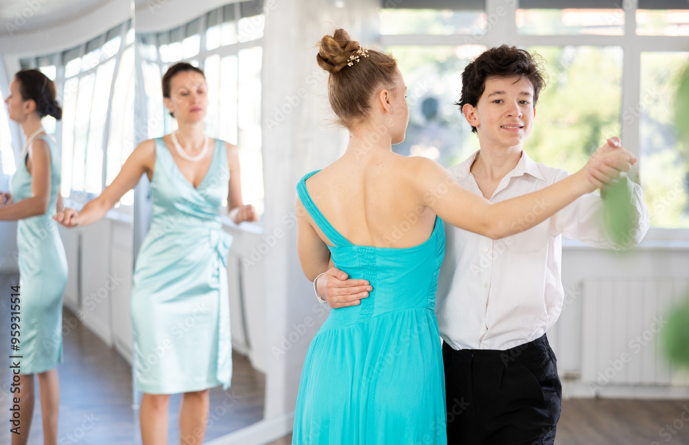 Obraz premium Passionate young ballroom enthusiasts, teenage girl and boy practicing graceful waltz routine in well-lit dance hall under female mentor watchful eye