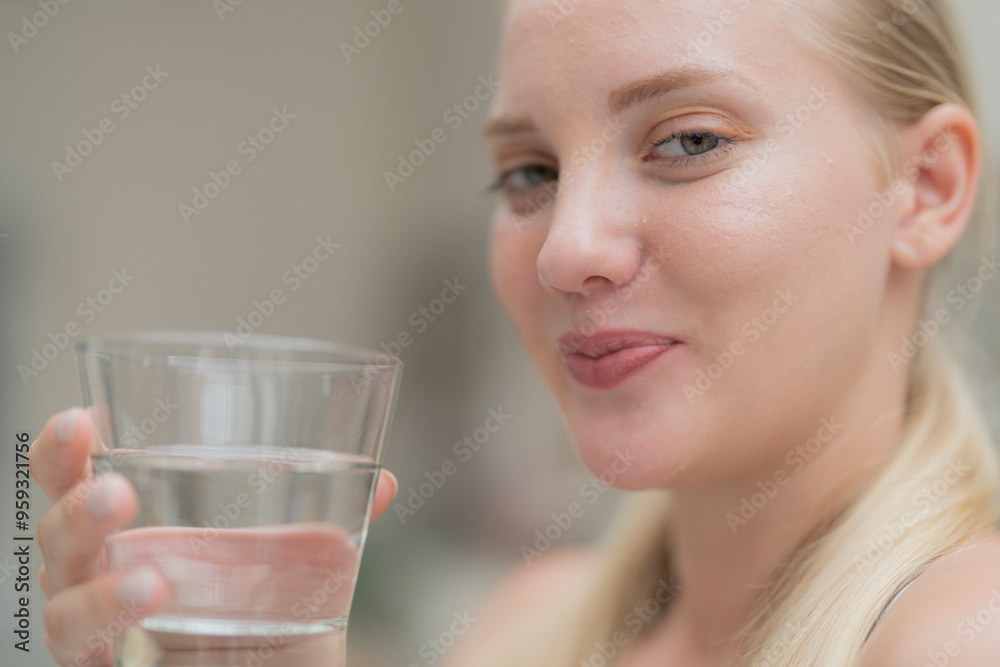 A beautiful European woman smiles happily, holding a glass of water, drinking natural mineral water from a clear glass, inside a residential. A healthy woman shows her face, complete physical health. A beautiful European woman smiles happily, holding a glass of water, drinking natural mineral water from a clear glass, inside a residential. A healthy woman shows her face, complete physical health.