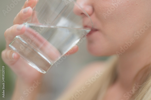 A beautiful European woman smiles happily, holding a glass of water, drinking natural mineral water from a clear glass, inside a residential. A healthy woman shows her face, complete physical health.