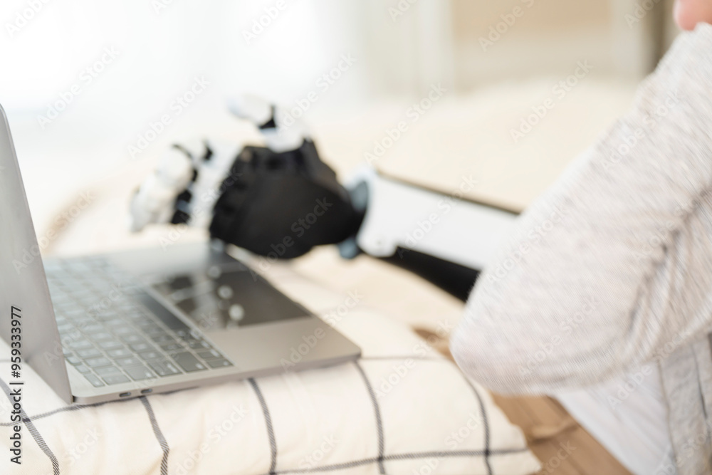 © ultramansk - A young woman is using a robotic prosthetic arm hand attached to her body to work on a desk. she is doing computer document and communication work. woman tries to control the smart arm in her home.