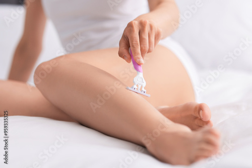 Woman shaving leg on bed, closeup. Depilation procedure