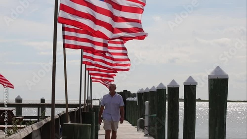 Crisfield, Maryland, USA A man walks on a pier on the Chesapeake Bay shore with American flags flying in the wind.  photo