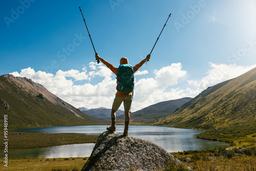 Cheering woman backpacker hiking on high altitude mountain top,with a lake in the distance