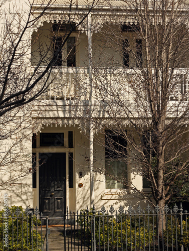 White Victorian style house with balcony decorated by intricate white ironwork is partially shaded by bare trees in the front yard, St Kilda, Melbourne, Australia photo