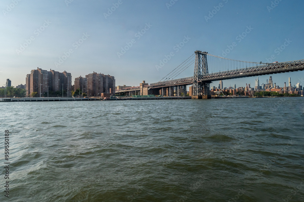 Taken from a ferry on the way to New York City, this picturesque view captures the calm waters, with the city's towering skyline illuminated by the city's lights. The Manhattan Bridge stands prominent Taken from a ferry on the way to New York City, this picturesque view captures the calm waters, with the city's towering skyline illuminated by the city's lights. The Manhattan Bridge stands prominent