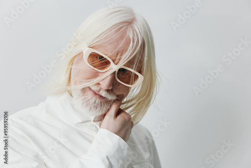 Elderly man with long white hair wearing sunglasses and a white shirt, exuding a thoughtful and playful attitude in a minimalistic background