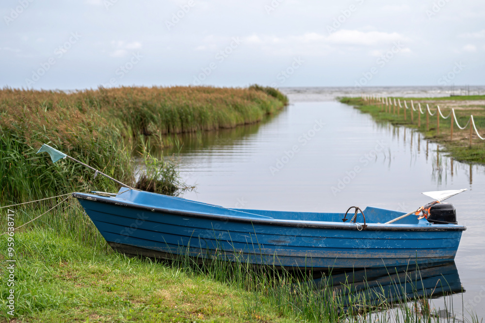 A blue boat rests on still water with lush green grass nearby under a clear sky. A blue boat rests on still water with lush green grass nearby under a clear sky.