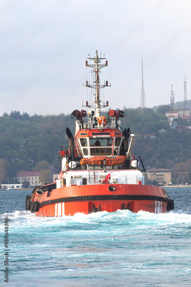 Fototapeta premium Orange tugboat sailing in the Bosphorus. The pilot boat leaves leaving foam behind. Marine craft idea concept.
