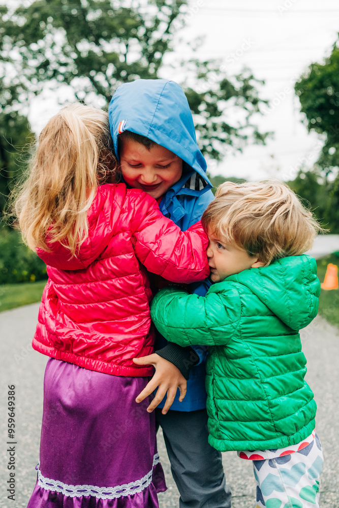 Three children hugging on a road, dressed in colorful jackets Three children hugging on a road, dressed in colorful jackets