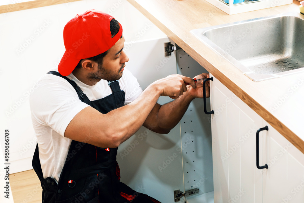 Asian professional plumber man work in a uniform fixing a broken water pipe problem under the sink in the client kitchen house. Indoor sink leaky repairing service. Home improvement concept. Asian professional plumber man work in a uniform fixing a broken water pipe problem under the sink in the client kitchen house. Indoor sink leaky repairing service. Home improvement concept.