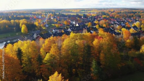 Smooth aerial footage gliding over a colorful autumn forest and a quaint town, capturing the vibrant fall colors in a stunning seasonal display