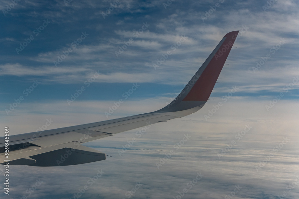 Obraz premium Wing of an airplane flying above the clouds in the blue sky.