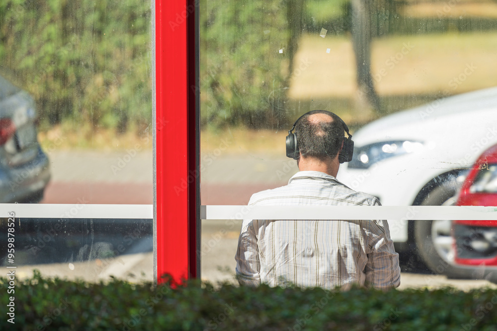 Ein Mann sitzt mit Kopfhörern an einer Bushaltestelle