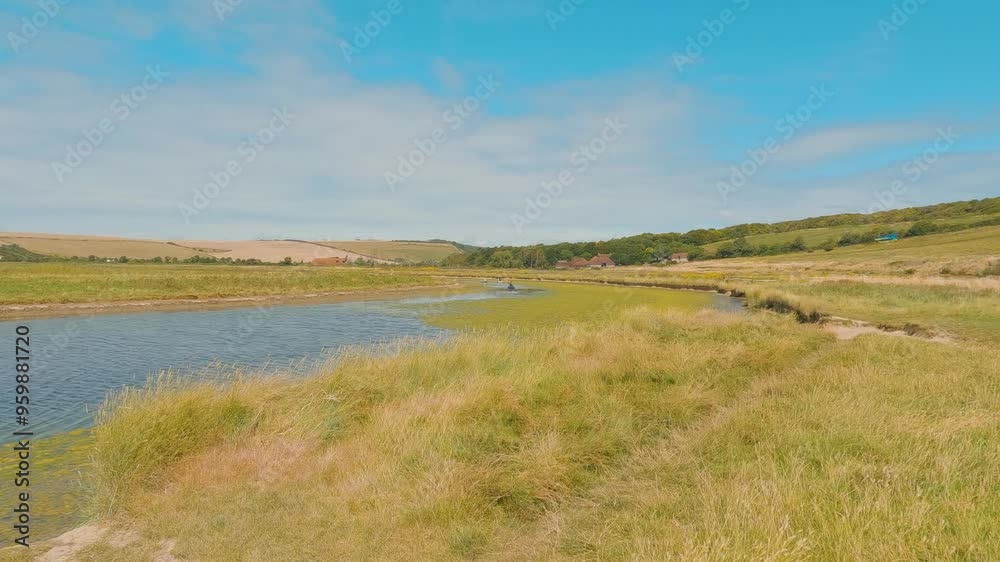 A river flows on the meadows of Newhaven. A person on a kayak is sailing on the river on a summer day A river flows on the meadows of Newhaven. A person on a kayak is sailing on the river on a summer day