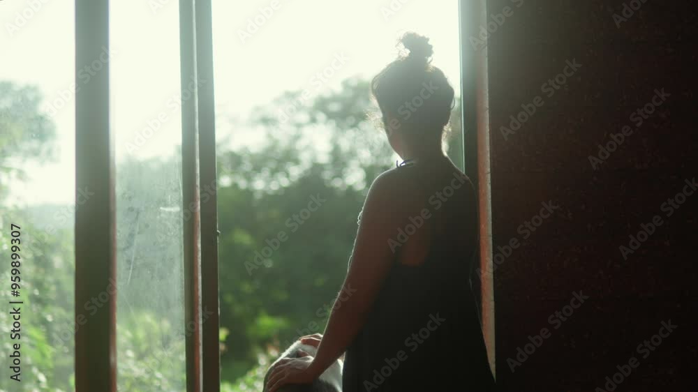 Woman and her dog stand at an open doorway, gazing outside at lush greenery in the soft light of the evening Woman and her dog stand at an open doorway, gazing outside at lush greenery in the soft light of the evening