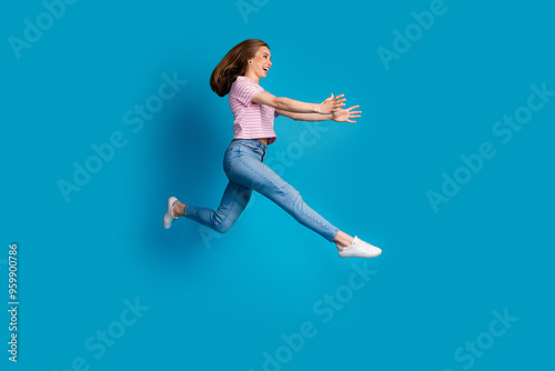 Full body photo of attractive young woman running catch empty space welcome dressed striped pink clothes isolated on blue color background