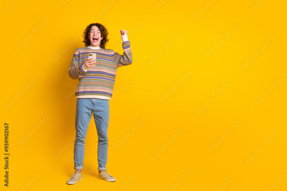 Full size photo of overjoyed guy dressed ornament sweater hold smartphone win betting scream yeah isolated on yellow color background Full size photo of overjoyed guy dressed ornament sweater hold smartphone win betting scream yeah isolated on yellow color background