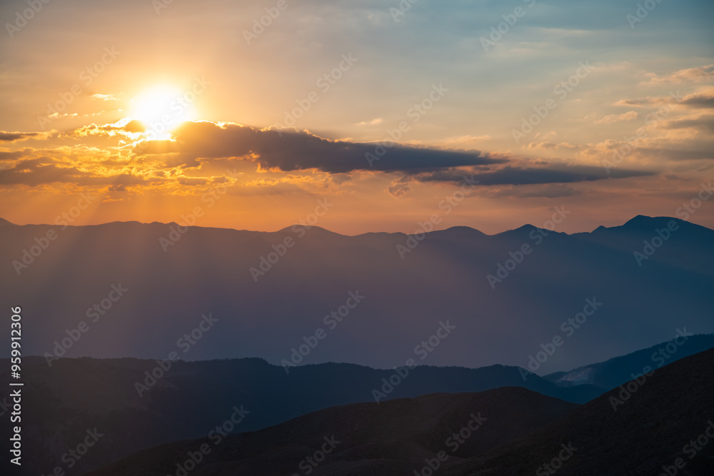 Obraz premium The setting sun over the mountains, the beautiful sun's rays shine through the clouds, the natural background, freedom, tranquility and peace