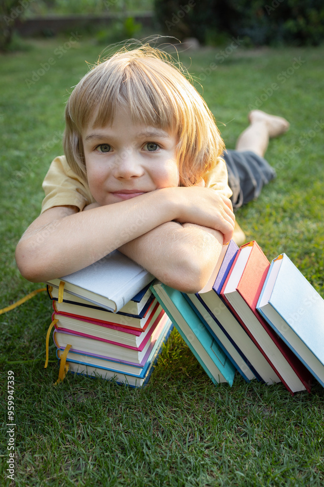 cute boy put his head on a stack of books while lying on the grass. back to school. Book Day. Read with pleasure. Education, development of imagination cute boy put his head on a stack of books while lying on the grass. back to school. Book Day. Read with pleasure. Education, development of imagination