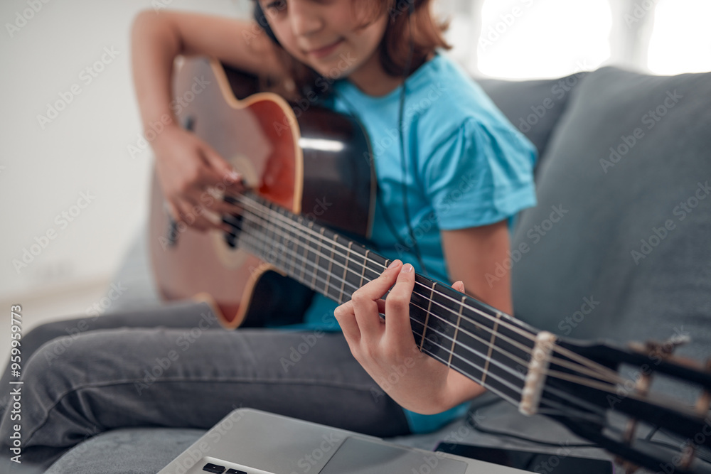 Fototapeta premium Kid playing guitar and watching video lessons on a laptop.
