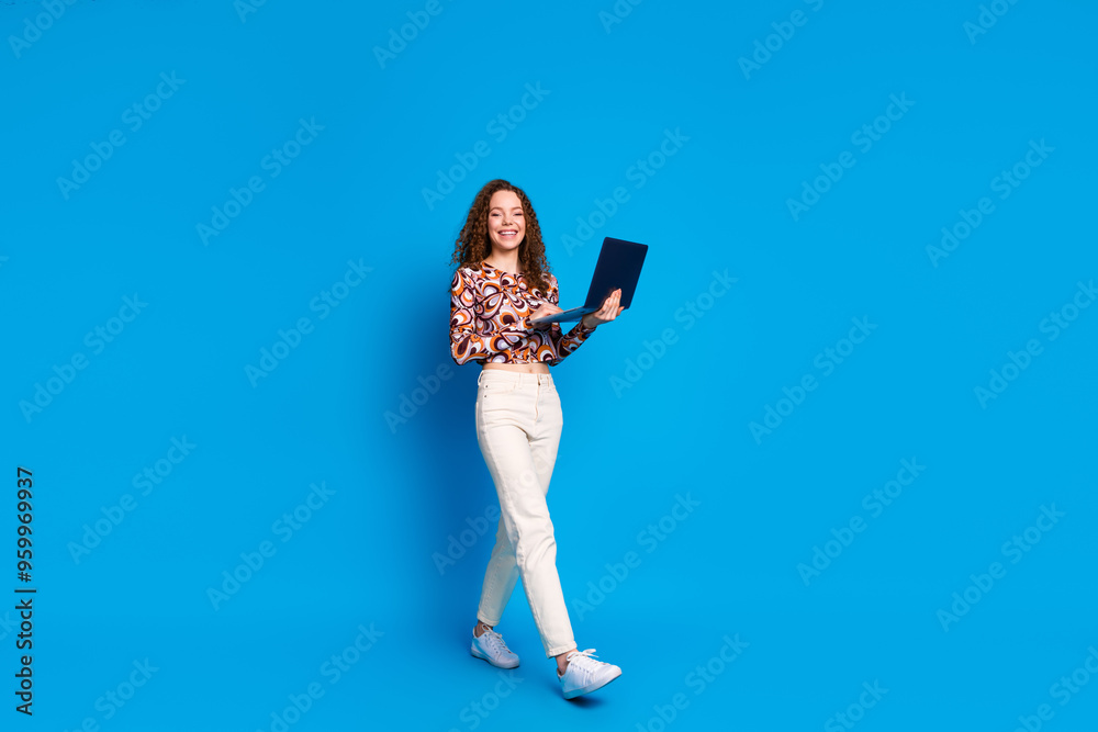 Full body photo of attractive young woman hold netbook walking dressed stylish colorful clothes isolated on blue color background Full body photo of attractive young woman hold netbook walking dressed stylish colorful clothes isolated on blue color background