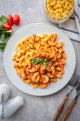 Stir fried macaroni with tomato sauce and egg in a white plate with fork and spoon, top view food table