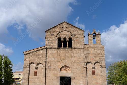 The front view of the Basilica of San Simplicio, a historic Romanesque church located in Olbia, Sardinia, Italy. Stonework ancient facade, arched windows, and a bell tower under a blue sky