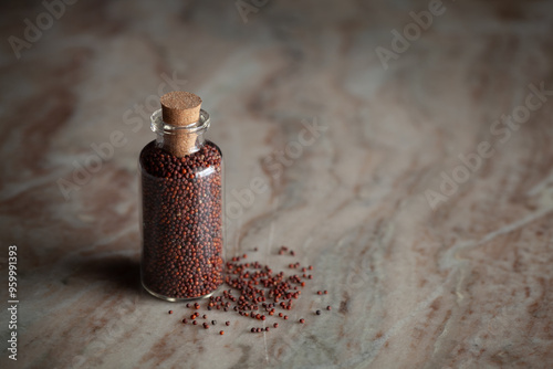 A small glass bottle filled with organic Ragi (Eleusine coracana) or finger millet is placed on a marble background. photo