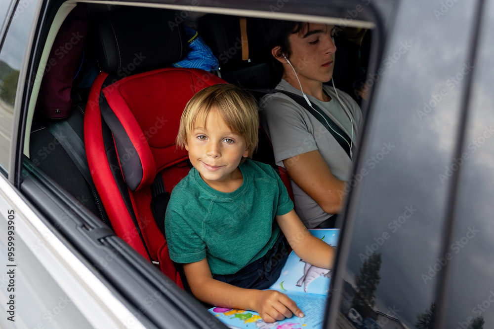 Children, boy siblings, traveling to vacation with car, sitting in carseats and reading books and playing Children, boy siblings, traveling to vacation with car, sitting in carseats and reading books and playing