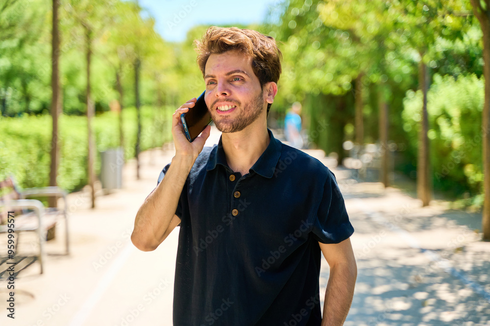 Obraz premium A man is talking on his cell phone while walking down a path. He is smiling and he is enjoying his conversation