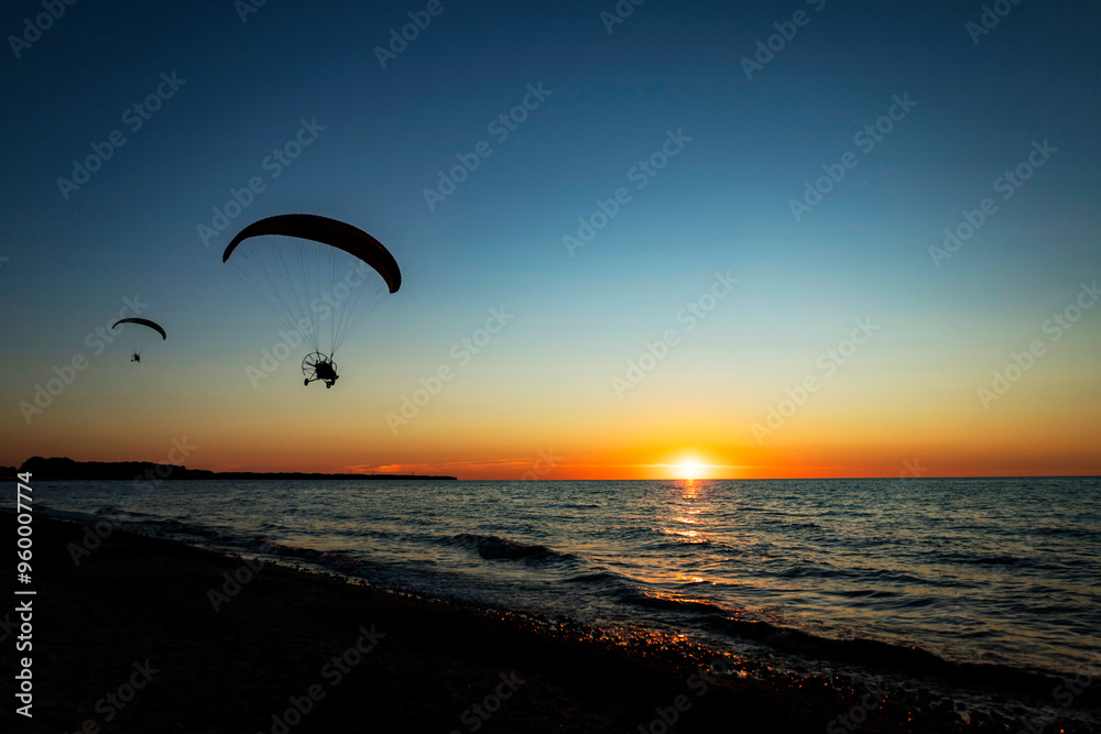 A person is joyfully parasailing high above the ocean during sunset