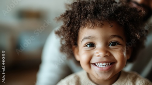 A close-up portrait of a young child with a brilliant smile, radiating happiness and innocence, taken in an indoor setting filled with cozy, warm lighting.