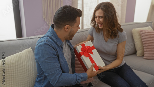 Wallpaper Mural Couple sharing a gift in a cozy home setting with a woman smiling and a man handing over a wrapped present on a comfortable couch in the living room Torontodigital.ca
