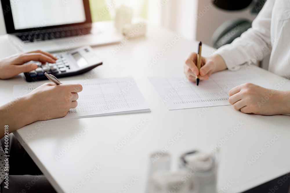 Two accountants using a calculator and laptop computer for counting taxes or revenue balance while rolls of receipts are waiting to be calculating. Business audit and taxes concepts Two accountants using a calculator and laptop computer for counting taxes or revenue balance while rolls of receipts are waiting to be calculating. Business audit and taxes concepts