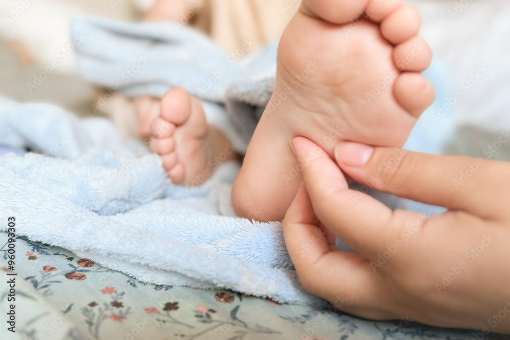 The mother tickles the baby's feet. Children's feet in the hands of the mother, wrapped in a blue blanket. Close-up of a todler's legs on a woman's hands. Mom and her child. Happy family concept The mother tickles the baby's feet. Children's feet in the hands of the mother, wrapped in a blue blanket. Close-up of a todler's legs on a woman's hands. Mom and her child. Happy family concept