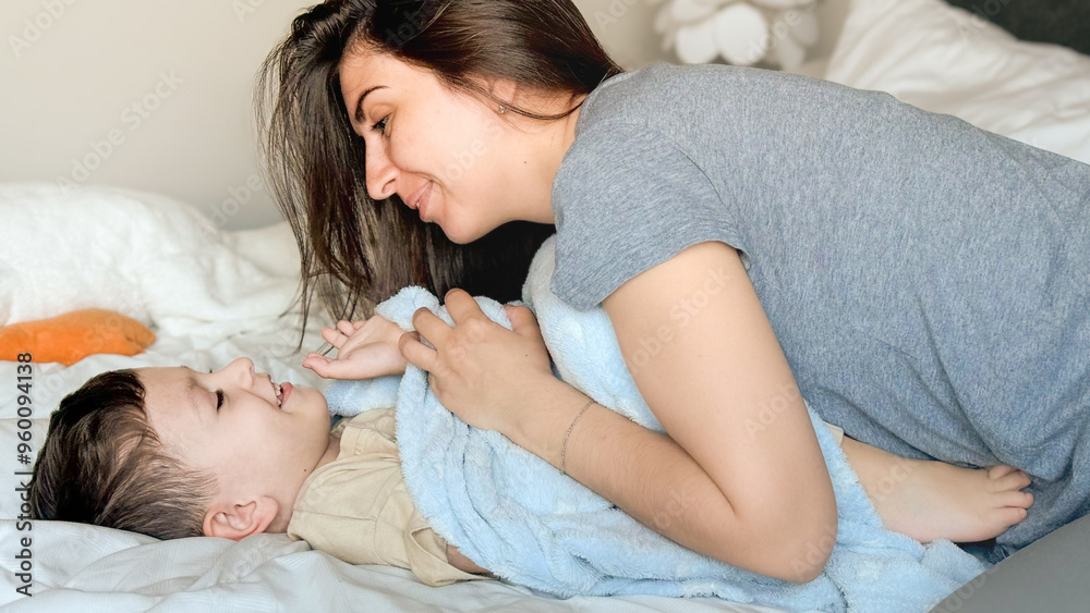A young mother in casual clothes plays tickle with her happy little son. Mom and child have fun together in a cozy bedroom at home. Happy children with mother. A young mother in casual clothes plays tickle with her happy little son. Mom and child have fun together in a cozy bedroom at home. Happy children with mother.