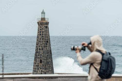 Male photographer taking pictures of the breaking waves at a lighthouse