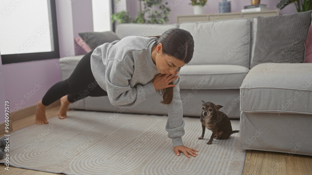 A young woman exercises in her living room with a chihuahua watching her closely. A young woman exercises in her living room with a chihuahua watching her closely.