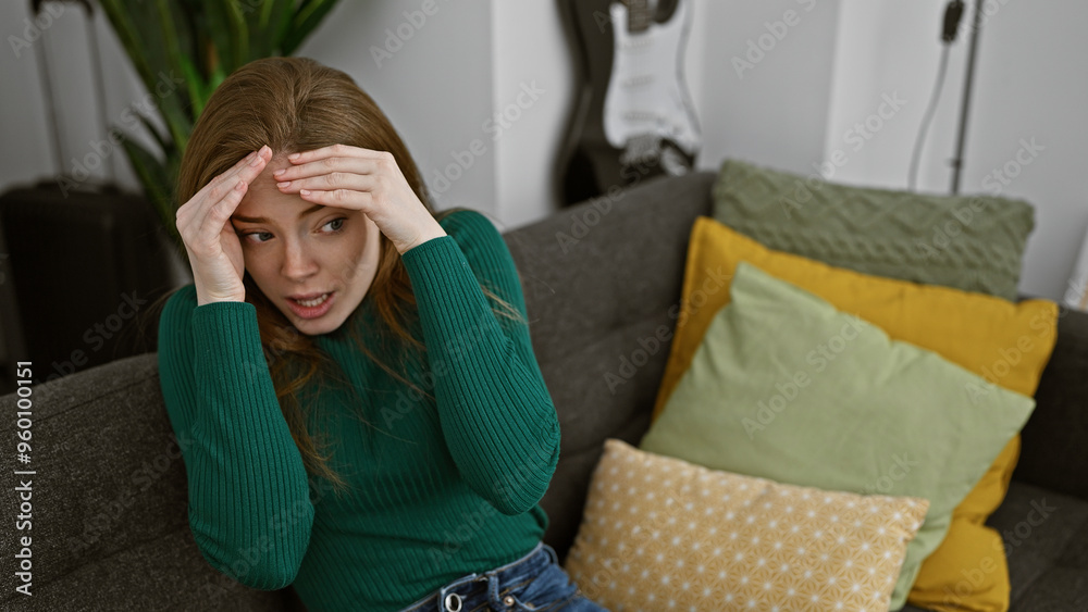 Obraz premium A concerned young woman sits on a sofa surrounded by colorful pillows in a cozy home setting, expressing worry or confusion.