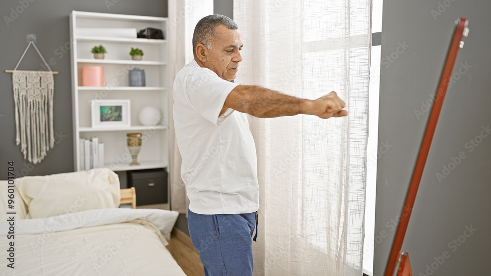Middle-aged hispanic man stretching in a modern bedroom setting with bookshelf and decor Middle-aged hispanic man stretching in a modern bedroom setting with bookshelf and decor