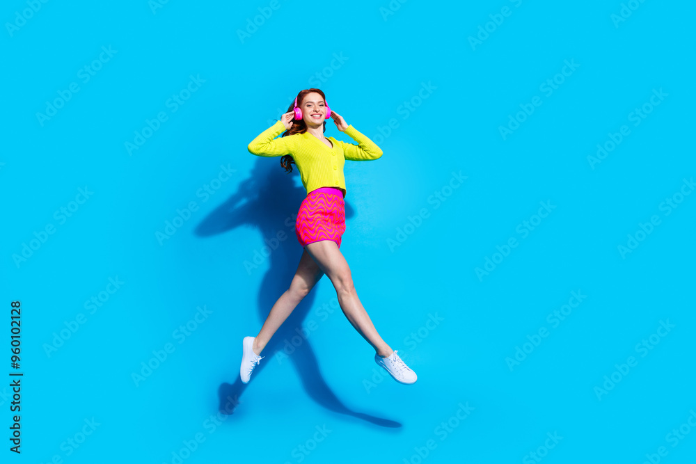 Full length photo of lovely young lady running listen music headphones dressed stylish yellow garment isolated on blue color background Full length photo of lovely young lady running listen music headphones dressed stylish yellow garment isolated on blue color background